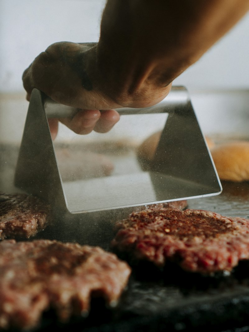 Burger patties being pressed on a hot grill